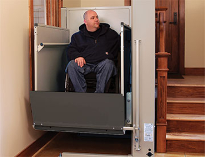 man using a vertical platform wheelchair lift to access main floor level of his home